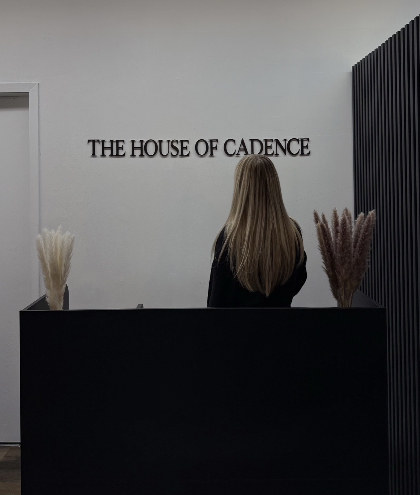 Abby at the front desk of The House of Cadence, facing the salon sign