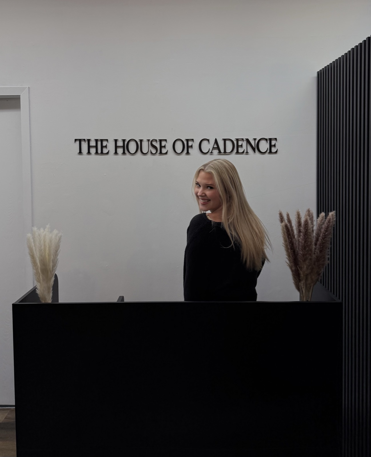 Abby at the front desk of The House of Cadence, under the salon sign
